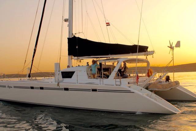 sunset and a white catamaran motoring along with the crew in the cockpit waving