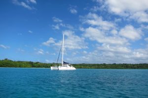 blue sea and sky with just a few clouds and a white yacht anchored next to a low green island