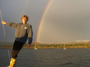 Bruce smiling on deck at Easter Island with a beautiful rainbow across the land behind