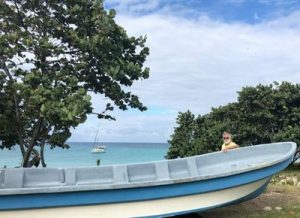 author brian simm next to a local pirogue on the beach with his boat at anchor behind