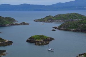 a scottish loch with small islands and a boat anchored alone - the dark mountains on the isle of skye in the background