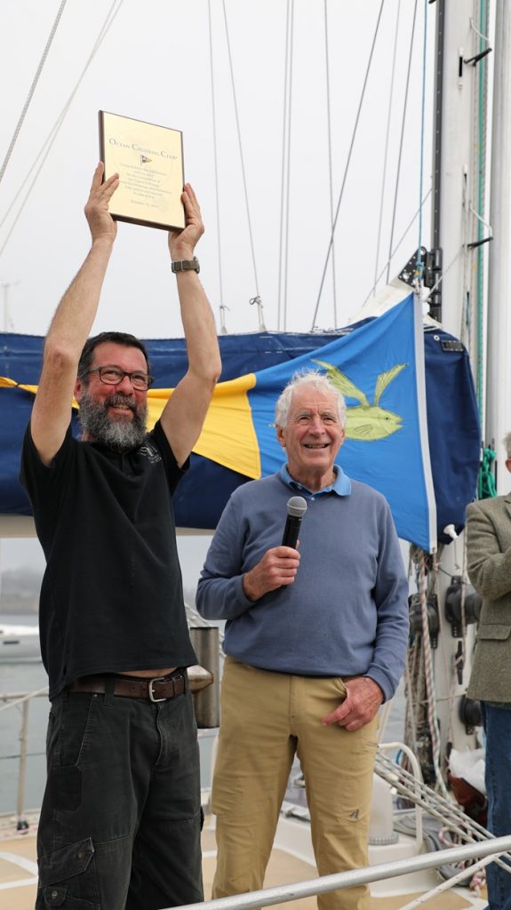 Randall dressed in a black t shirt with a thick grey beard holds the trophy high above his head