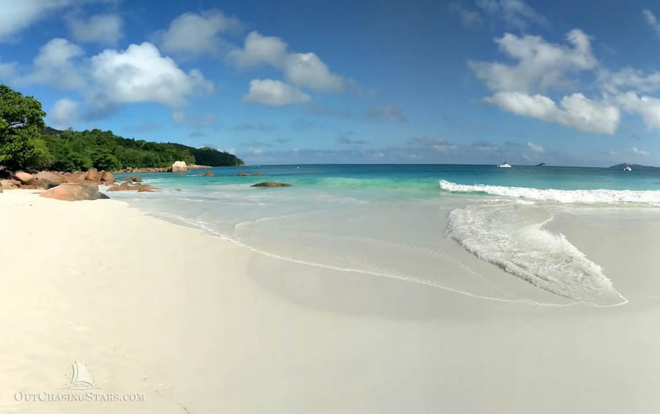 beautiful arc of a white sandy beach with surf coming in and a turquoise blue sea with boats anchored off