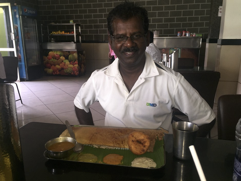 local man very dark with a moustache and white open necked shirt sitting in a diner facing the camera with his lunch on a tray in front of him