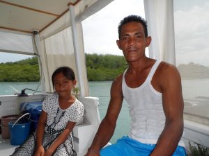 on the left a young local girl with her hair tied back and wearing a white dress and on the right her father wearing a white vest and blue shorts