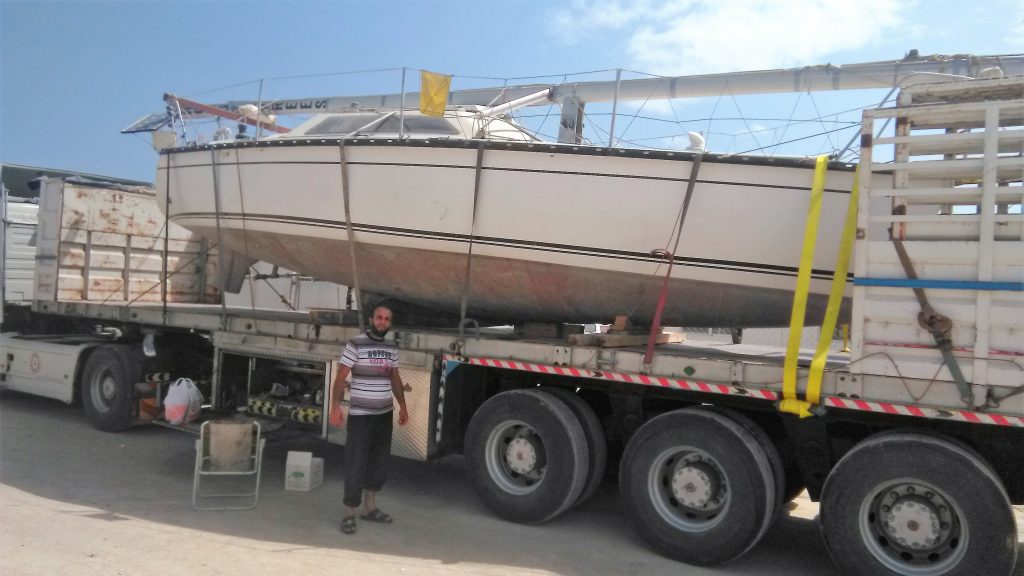 a boat on the back of a big lorry with tied downs and a local man in front, perhaps the driver