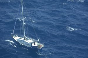 choppy seas and an aerial view looking down on a small blue hulled yacht with no sails up drifting