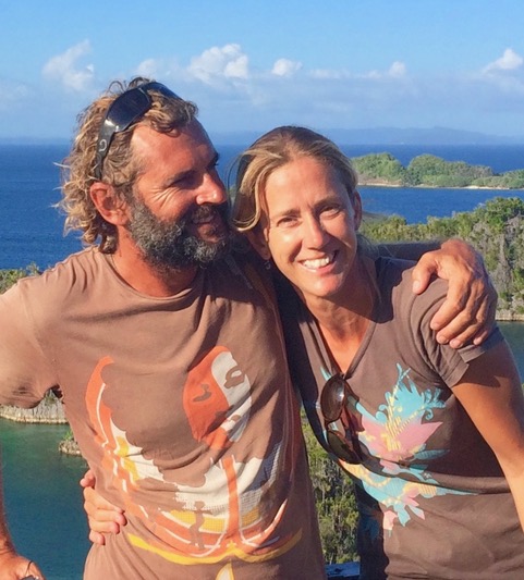 a couple in matching brown t shirts tanned and healthy with their arms around each other smiling at the camera