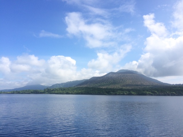 an island with green vegetation around the coats an more arid slopes rising to gently sloping mountains