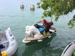 a man in a red shirt driving a dinghy crouching with the dinghy full of plastic rubbish bags