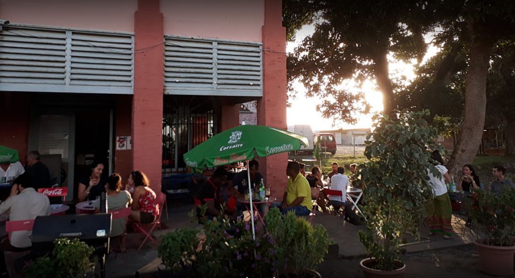 ;pink building with a green umbrella and people sitting outside on chairs at tables