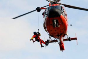 Helicopter lowering a person on a winch cable.